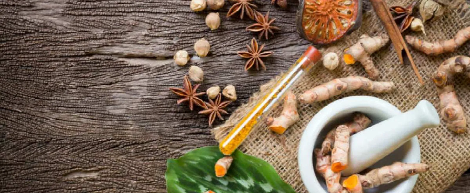 Ayurvedic ingredients including turmeric root, star anise and a mortar and pestle on a wooden table