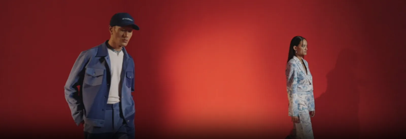 Muvazo campaign video still of two models in denim and printed co-ords against a red backdrop